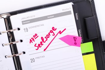 Seelsorge in besonderen Bereichen In einem Terminplaner ist eine Seite aufgeschlagen, auf der mit roter Farbe und verstärkt durch einen Klebepfeil als Termin „17.00 Uhr Seelsorge“ eingetragen ist