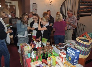 Faire-Woche Auf einem Tisch stehen viele verschiedene, fair gehandelte Produkte; dahinter stehen Menschen, die sich angeregt unterhalten